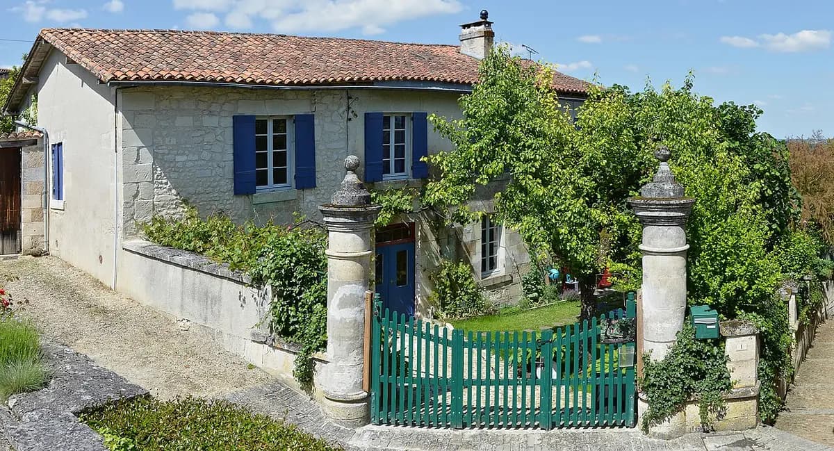 Casa antigua de piedra con contraventanas azules y verja verde en Aubeterre-sur-Dronne, Charente