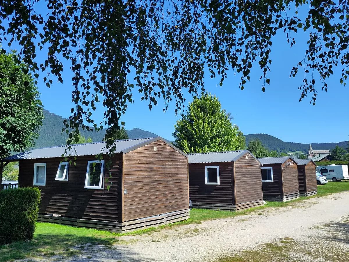 Hilera de mobil-homes de madera en un camping de montaña, bajo un cielo azul