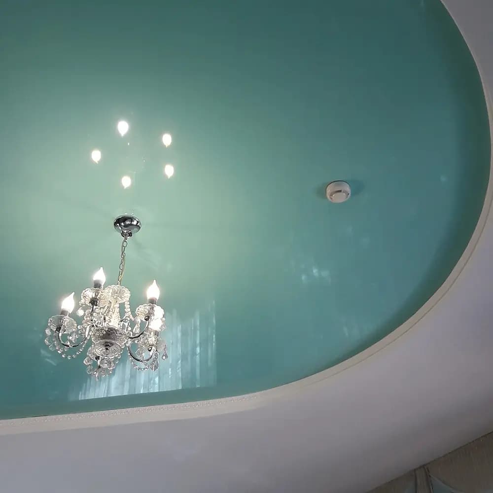 Plafond van een woonkamer met een witte rookmelder bij een kroonluchter